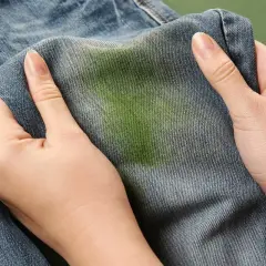Dłonie trzymają dżinsy z zieloną plamą po trawie. Zastanawiasz się, czym sprać trawę z ulubionych spodni?