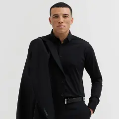 Mężczyzna w czarnym garniturze, z marynarką na ramieniu. Czarny pasek do garnituru z metalową klamrą podkreśla elegancką stylizację.