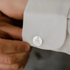 Mężczyzna zapina spinki do mankietów koszuli. Na spinkach widnieje kotwica i inicjały PM. To prosty sposób, jak zapiąć spinki do koszuli.