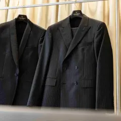 Dwa eleganckie garnitury wiszą na wieszakach. Jeden w prążki, drugi z subtelnym wzorem. Prasowanie garnituru to klucz do nienagannego wyglądu.