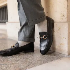 Szare, gładkie skarpetki do mokasynów z czarnymi, lakierowanymi butami i złotą klamrą. Elegancka stylizacja.