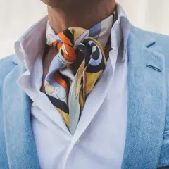 Elegancki mężczyzna w błękitnej marynarce i białej koszuli, z kolorowym fulararem zawiązanym pod szyją.