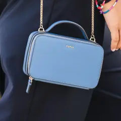 Niebieska torebka Furla z złotym logo, noszona na złotym łańcuszku. Torebka jest częścią stylizacji, która podkreśla, furla co to za marka.