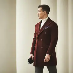 Elegancki mężczyzna w bordowej bosmance i białym golfie, z czarnymi rękawiczkami w dłoni, spogląda w bok.