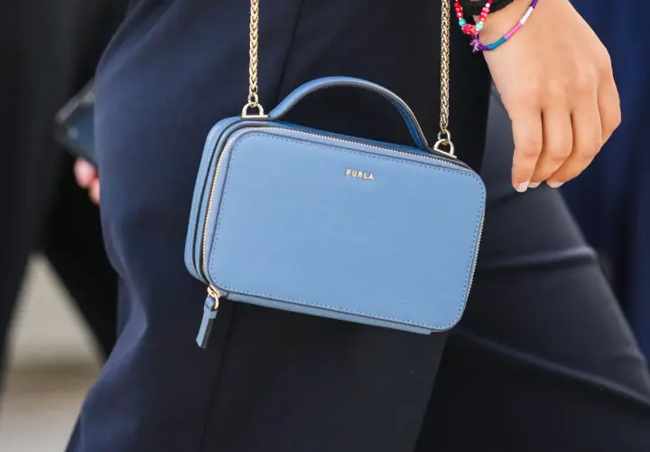 Niebieska torebka Furla z złotym logo, noszona na złotym łańcuszku. Torebka jest częścią stylizacji, która podkreśla, furla co to za marka.