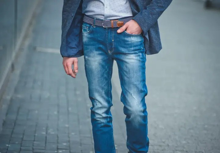 Mężczyzna w niebieskiej marynarce i modnych jeansach, prezentujący różne rodzaje spodni męskich.