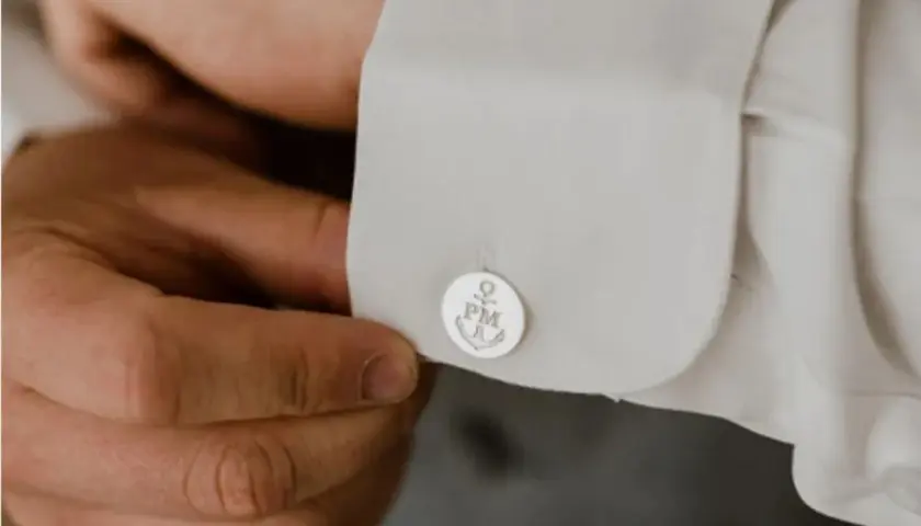 Mężczyzna zapina spinki do mankietów koszuli. Na spinkach widnieje kotwica i inicjały PM. To prosty sposób, jak zapiąć spinki do koszuli.
