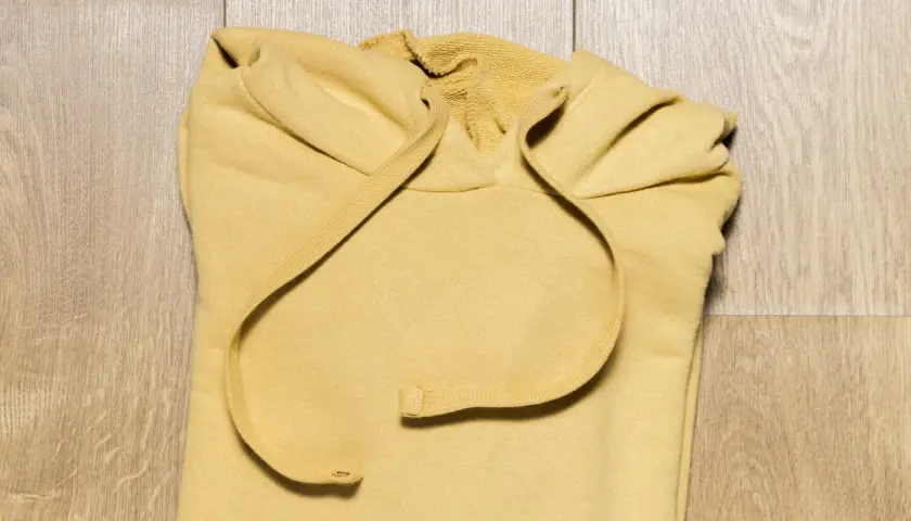 Żółta bluza z kapturem złożona na drewnianym tle.