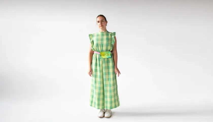 Kobieta w zielonym kombinezonie w kratkę, z kolorową nerką na biodrach, na białym tle.