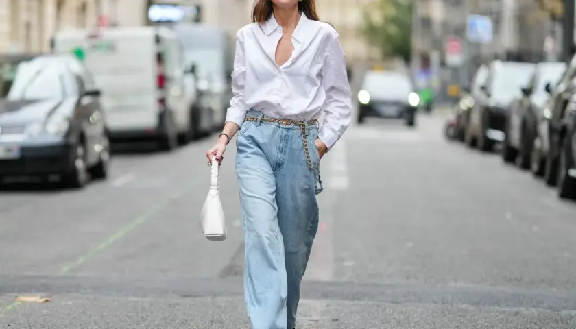 Kobieta w luźnych, jasnych jeansach typu mom fit i białej koszuli, z białą torebką. Stylizacja dla każdej kobiety ceniącej wygodę i modny wygląd.