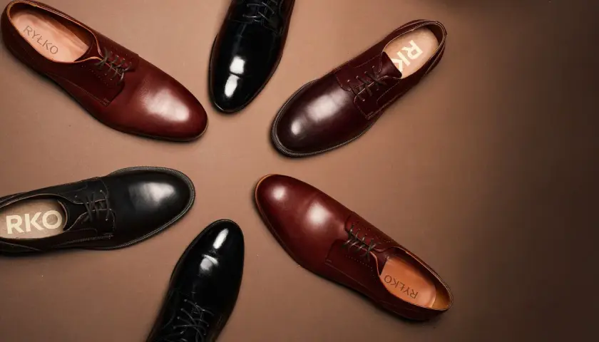 Eleganckie brązowe buty do czarnego garnituru i czarne lakierki, obie pary od Ryłko, ułożone na brązowym tle.