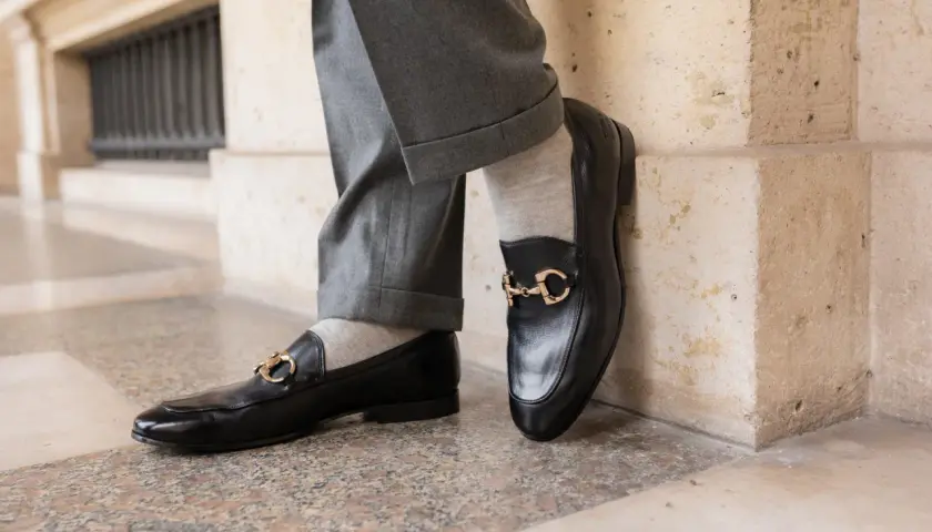 Szare, gładkie skarpetki do mokasynów z czarnymi, lakierowanymi butami i złotą klamrą. Elegancka stylizacja.