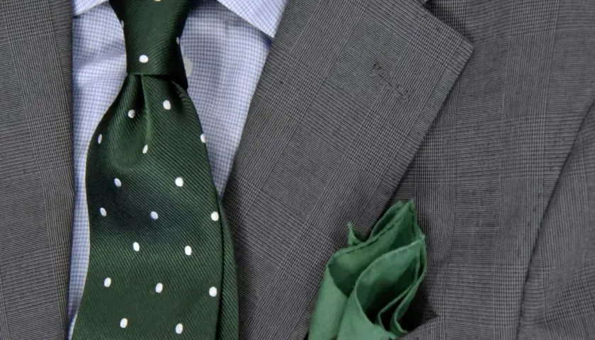 Elegancki zestaw: niebieska koszula, zielony krawat w groszki i szara marynarka. Idealna odpowiedź na pytanie: jaki krawat do niebieskiej koszuli.