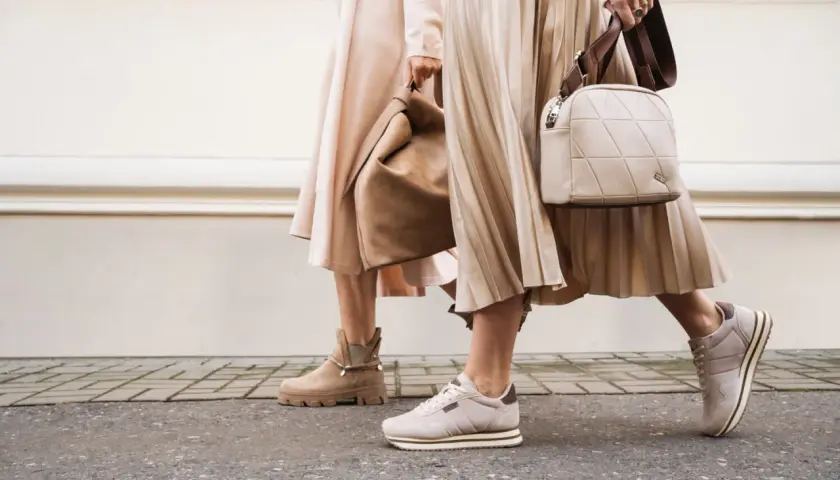 Dwie kobiety w beżowych sukienkach i butach. Jedna ma botki, druga sneakersy. Idealne połączenie: jakie buty do rajstop?