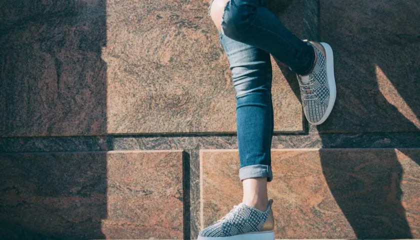 Dziewczyna w podartych jeansach i modnych sneakersach z wzorem pinroll opiera się o kamienną ścianę.
