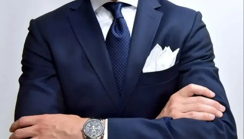 Elegancki mężczyzna w granatowym garniturze, białej koszuli i granatowym krawacie w kropki. Idealna inspiracja, jaki krawat do granatowej koszuli.