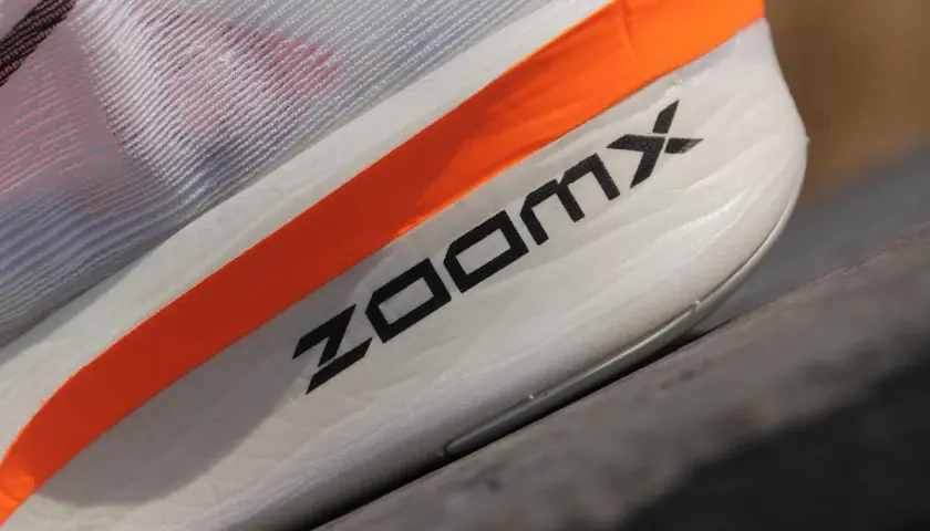 Biały but sportowy z pomarańczowym paskiem i napisem ZOOMX.