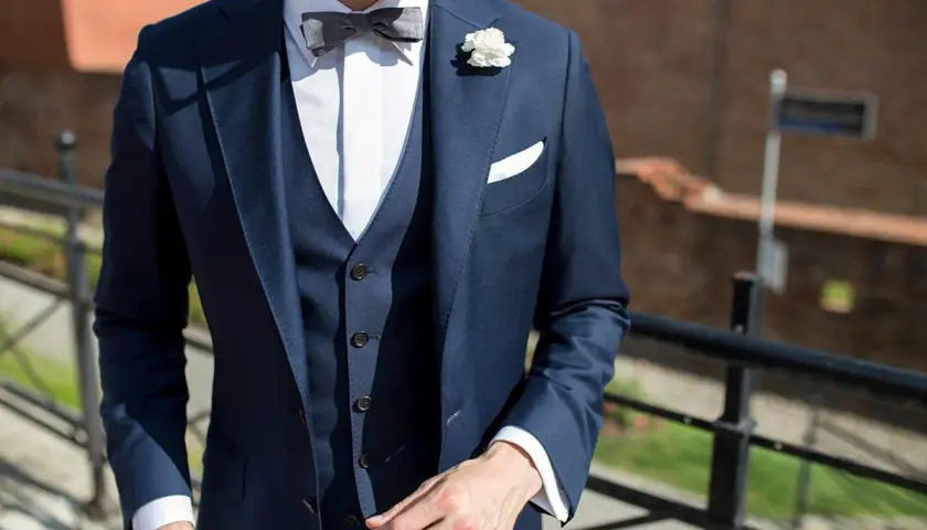 Eleganckie stylizacje z kamizelką pikowaną: granatowy garnitur, biała koszula, szara mucha i biała butonierka.