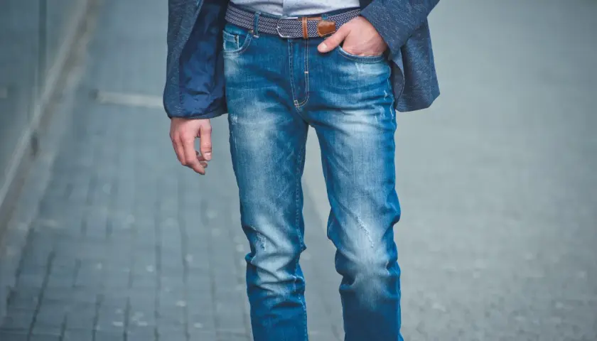 Mężczyzna w niebieskiej marynarce i modnych jeansach, prezentujący różne rodzaje spodni męskich.