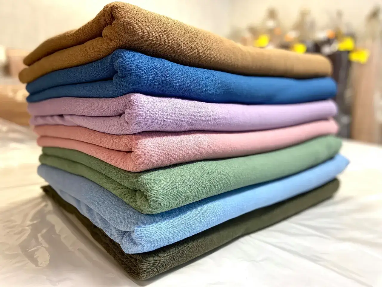 Stos kolorowych tkanin, od brązu po zieleń. To materiał typu jersey, miękki i elastyczny, idealny na ubrania.