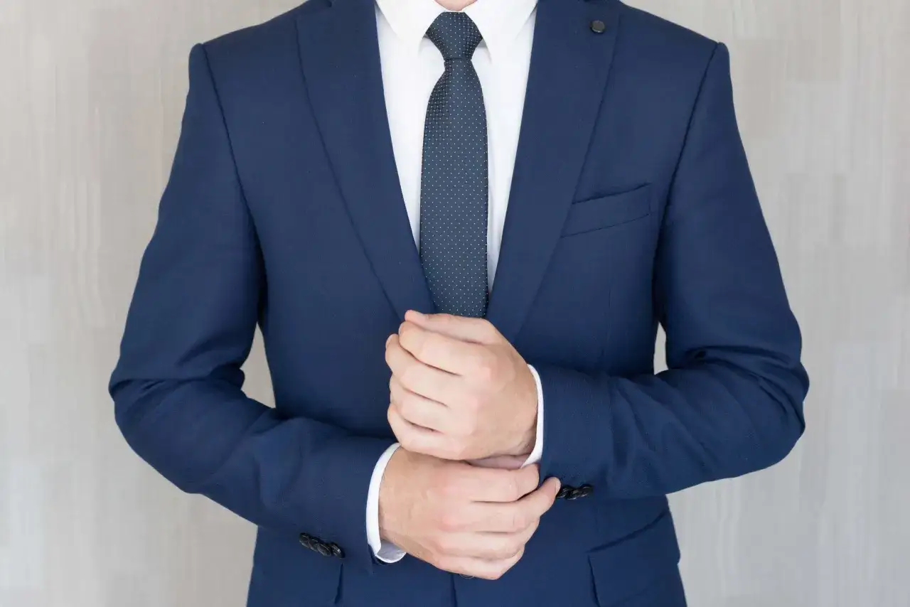 Elegancki mężczyzna w granatowym garniturze i białej koszuli, z granatowym krawatem w kropki. Idealny przykład, jaki krawat do granatowego garnituru.